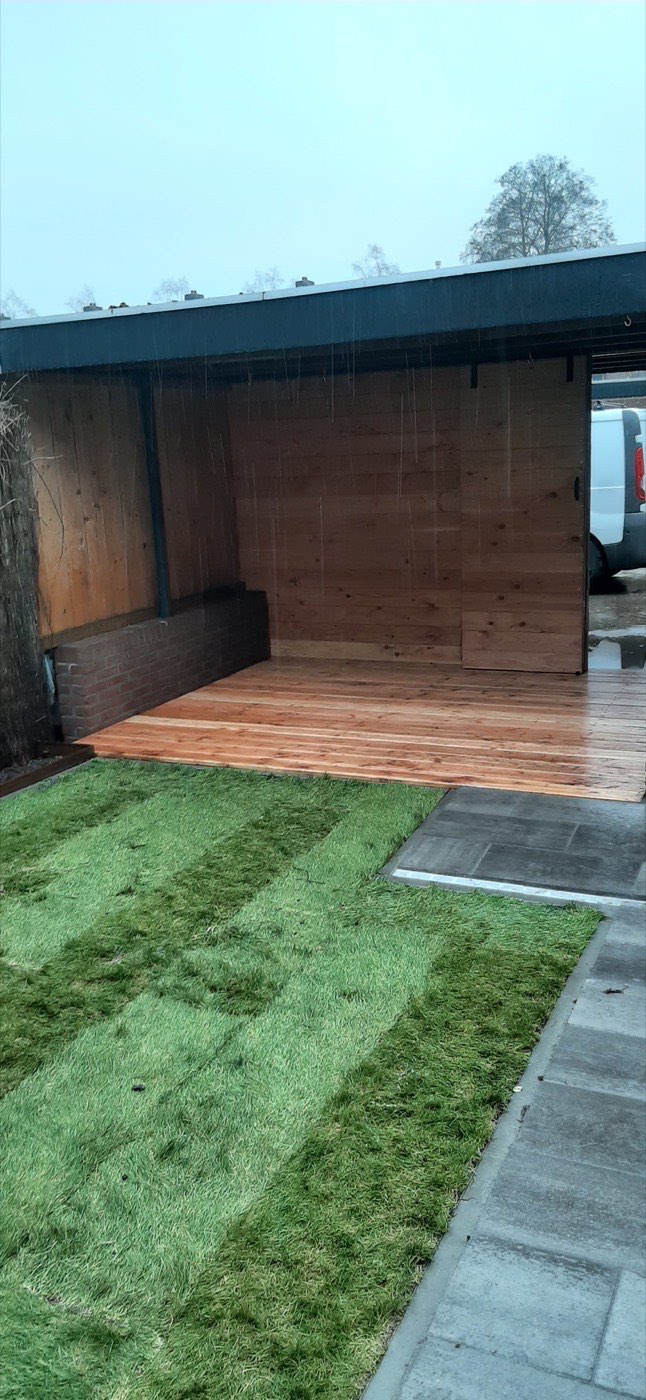 Nieuw aangelegd gestreept gazon bij een houten overkapping